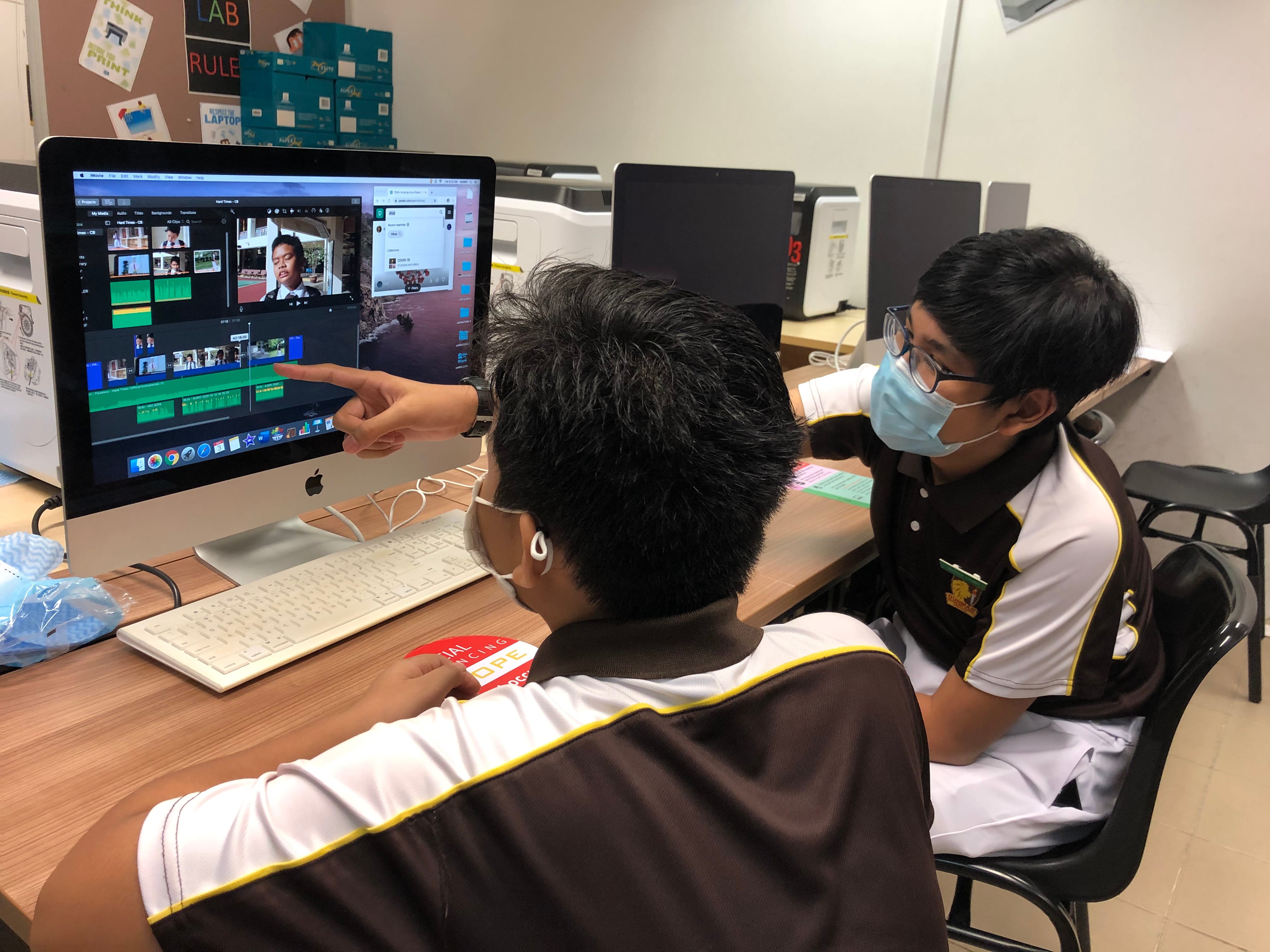 Two students in school uniforms collaborate on video editing software on an Apple iMac in a computer lab.